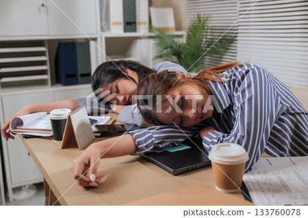 Young business women work online home office, team people exhaustion from business tasks, sleeping on desk, illustrating burnout, need vital rest from demanding workload, laptop and documents wait. Young business women work online home office, team people exhaustion from business tasks, sleeping on desk, illustrating burnout, need vital rest from demanding workload, laptop and documents wait. 133760078