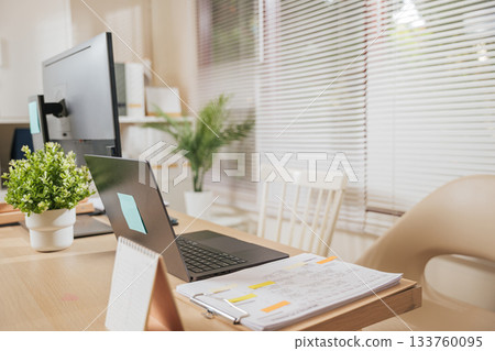 Home office workspace business desk setup provides laptop computer monitor documents calendar green plants creating efficient productive environment for remote work. 133760095