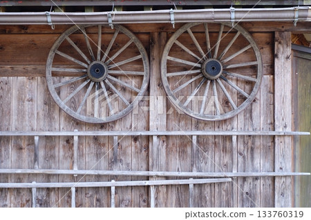 Wooden farm equipment wheels and ladders hang like eyes on the wall of an old house 133760319