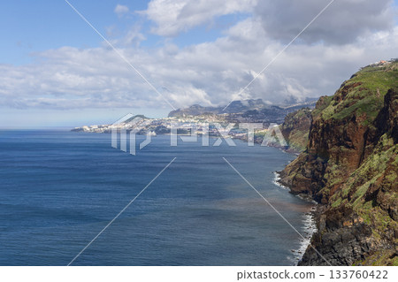 Garajau Madeira coastline with green slopes blue ocean and distant Funchal beneath glowing sky 133760422