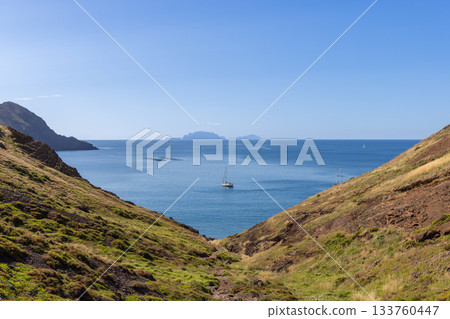 V shaped grassy slopes at Sao Lourenco in Madeira open to calm sea with yacht and islands 133760447