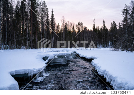 winter river flowing through snowy forest landscape in lapland 133760474