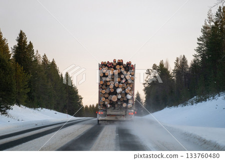 logging truck driving on snowy forest road in winter lapland 133760480