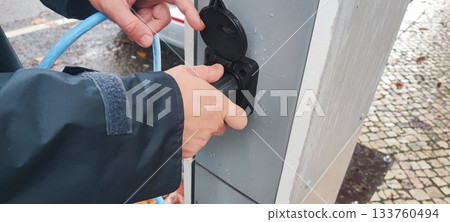 Human hand connecting an electric vehicle charging cable to a public charging station. Concept: electric vehicle infrastructure, clean energy, charging technology, eco-friendly transport. 133760494
