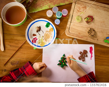 Child decorating clay Christmas tree and gingerbread figurines on paper 133761416