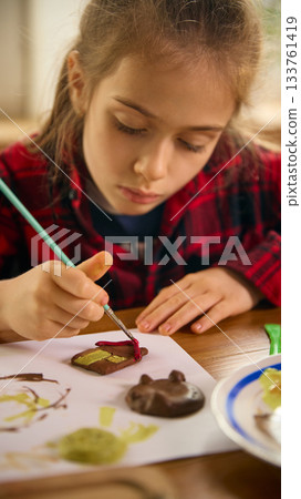 Girl painting small handmade clay house with focused expression 133761419