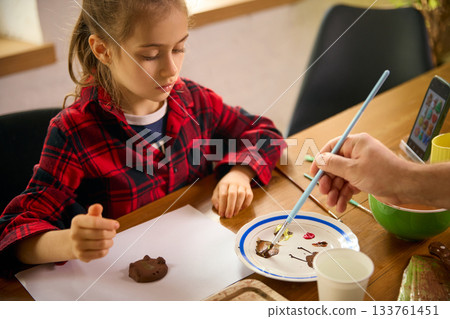 Girl preparing clay shape while father mixes paint for decoration Girl preparing clay shape while father mixes paint for decoration 133761451