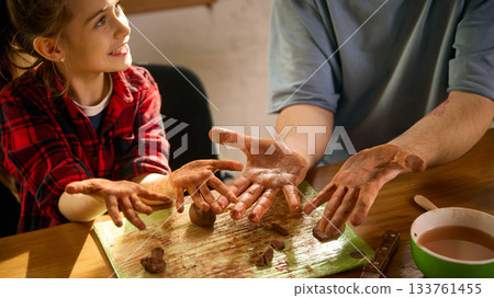 Girl showing muddy clay hands with father during sculpting practice 133761455