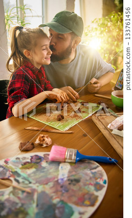 Father giving daughter affectionate kiss during clay crafting 133761456