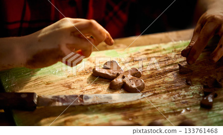 Hands shaping clay gingerbread figure on messy crafting board under warm daylight 133761468