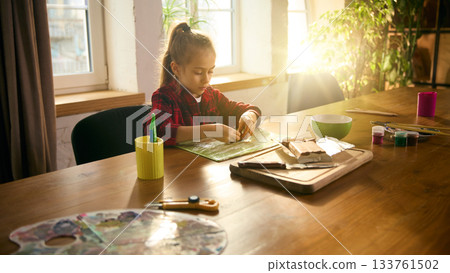 Girl shaping colorful clay at sunlit art table in warm creative home atmosphere 133761502