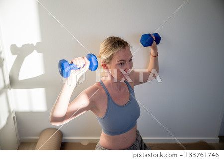 woman lifting dumbbells during home strength workout on yoga mat woman lifting dumbbells during home strength workout on yoga mat 133761746
