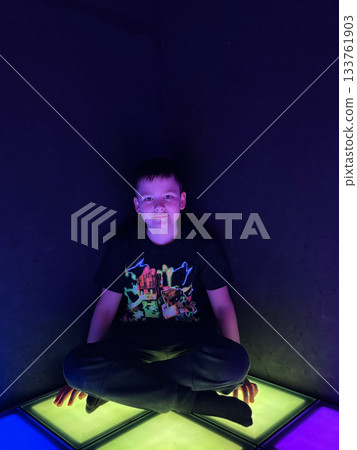 Young boy sitting in dark room, glowing light floor 133761903
