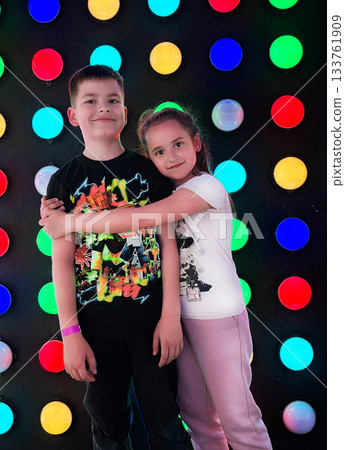 Siblings hugging smiling against colorful light wall Siblings hugging smiling against colorful light wall 133761909