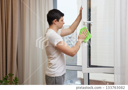 Man performing household chore, wiping down a residential window frame indoors 133763082