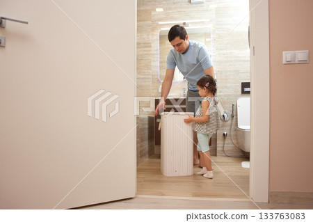 Father and daughter placing dirty clothes into a laundry hamper at home Father and daughter placing dirty clothes into a laundry hamper at home 133763083