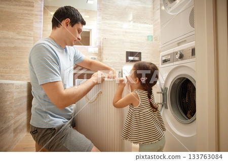 Father and daughter sorting clothes from the laundry basket in bathroom Father and daughter sorting clothes from the laundry basket in bathroom 133763084