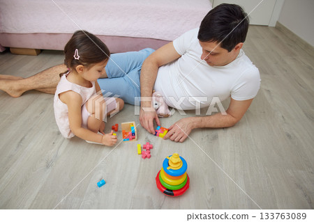 Father and daughter enjoying quality time together, playing with colorful building blocks on floor Father and daughter enjoying quality time together, playing with colorful building blocks on floor 133763089
