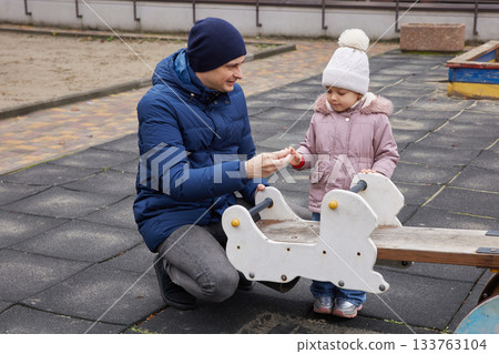 Father playing with toddler daughter on a seesaw at an outdoor playground in winter Father playing with toddler daughter on a seesaw at an outdoor playground in winter 133763104