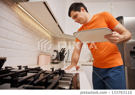 Man cleaning white kitchen countertop with sponge in a modern kitchen Man cleaning white kitchen countertop with sponge in a modern kitchen 133763118