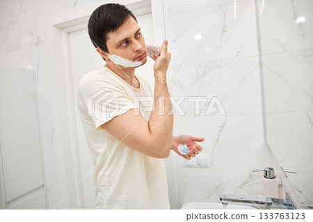 Man applying shaving foam to his face for a morning shave routine Man applying shaving foam to his face for a morning shave routine 133763123