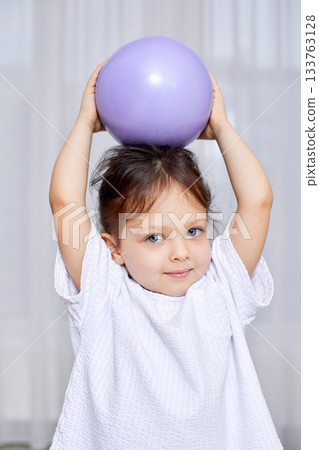Young girl balancing a purple ball on her head, showcasing childhood play and skill Young girl balancing a purple ball on her head, showcasing childhood play and skill 133763128