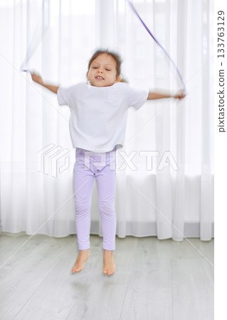 Child jumping rope, exercising and having fun indoors in a bright room Child jumping rope, exercising and having fun indoors in a bright room 133763129