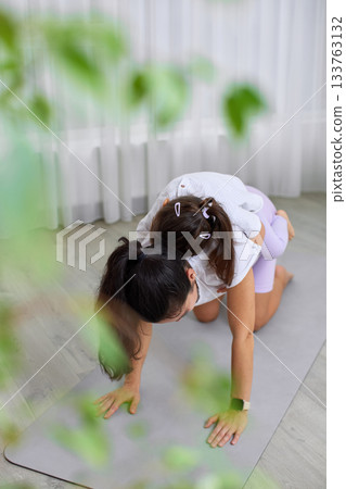Mother doing yoga pose with her daughter on her back at home 133763132