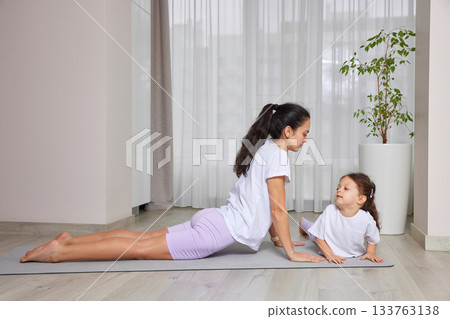 Mother and daughter practicing cobra pose on yoga mat, enjoying fitness and healthy lifestyle Mother and daughter practicing cobra pose on yoga mat, enjoying fitness and healthy lifestyle 133763138
