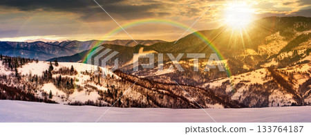 panorama with snowy forested hills in winter at sunset. beautiful landscape of mountain ridge with snow covered peaks in the distance in evening light. leadership corporate wallpaper under the rainbow panorama with snowy forested hills in winter at sunset. beautiful landscape of mountain ridge with snow covered peaks in the distance in evening light. leadership corporate wallpaper under the rainbow 133764187