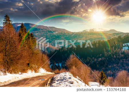 country road winding through winter landscape under blue sky at sunset. mountains in evening light. travel background with snow covered slopes. storytelling cinematic image under the rainbow country road winding through winter landscape under blue sky at sunset. mountains in evening light. travel background with snow covered slopes. storytelling cinematic image under the rainbow 133764188