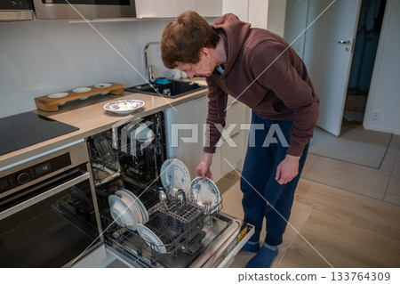 man unloading clean dishes from dishwasher in modern bright kitchen man unloading clean dishes from dishwasher in modern bright kitchen 133764309