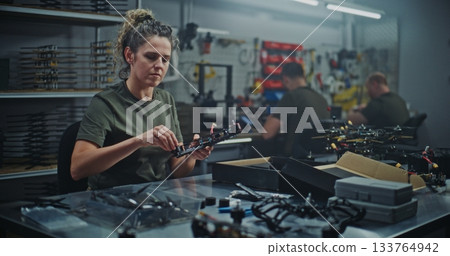 Female Technician Engaged in Hands on Assembly of Modern FPV drone, Connecting Small Parts Frame Female Technician Engaged in Hands on Assembly of Modern FPV drone, Connecting Small Parts Frame 133764942