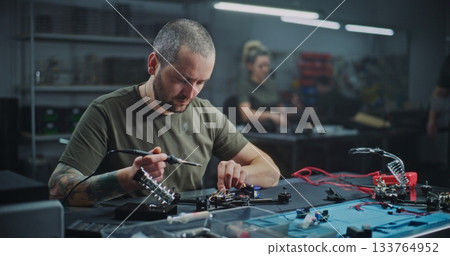 Adult Male Worker Closely Soldering Small Drone Component on Workbench Adult Male Worker Closely Soldering Small Drone Component on Workbench 133764952