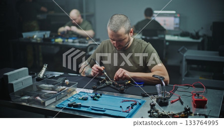 Technician Soldering Components on FPV Drone Circuit Board 133764995