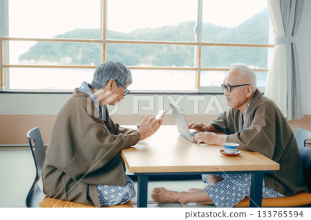 一對老年夫婦在日式旅館的房間裡使用電腦和智慧型手機。 133765594