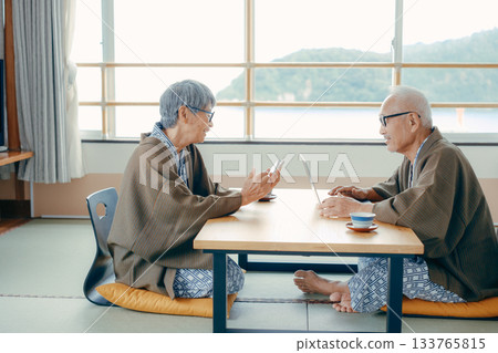 An elderly couple taking pictures of the scenery with their smartphones at a traditional Japanese inn 133765815