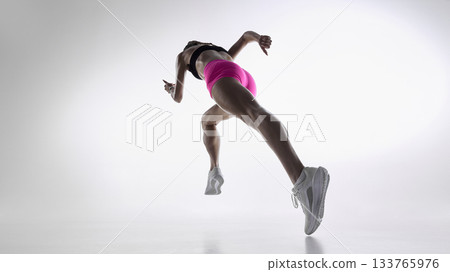 Dynamic rear low-angle shot of female runner accelerating in bright studio 133765976