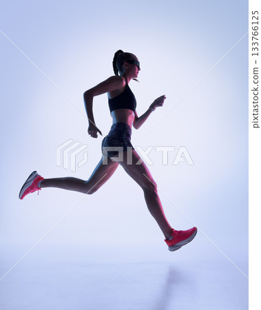 Female runner in neon studio jumping with strong athletic extension 133766125