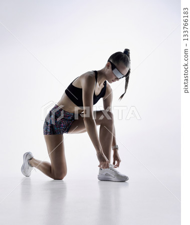 Athletic woman kneeling to tie running shoes before workout in studio 133766183