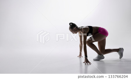 Female sprinter in starting position on minimal white background 133766204