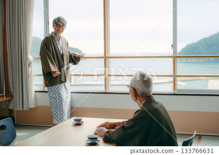 An inn scene with an elderly woman waving at the window and her husband watching over her. 133766631