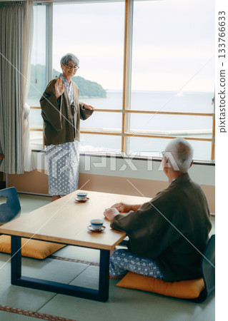 An inn scene with an elderly woman waving at the window and her husband watching over her. 133766633
