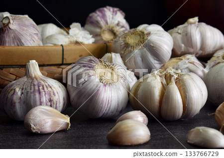 Close-up shot of garlic laying on black stone table and bamboo baskets In the dimly lit kitchen prepared for the ingredients of the meal. 133766729