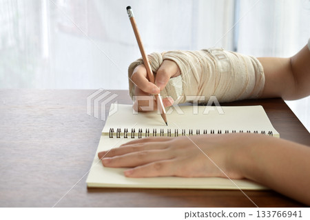 Person with broken arm injury doing physical therapy Rehabilitation by practicing hand drawing with pencil on paper. 133766941