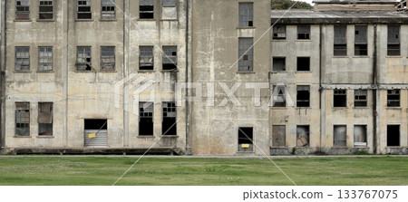An Old abandoned building facade architecture with broken window ,concrete surface and green lawn 133767075