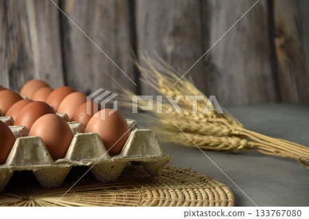 Eggs in a paper tray Placed on wicker and concrete floors. Garnish with dried barley. There is a background of blurry wooden planks. 133767080