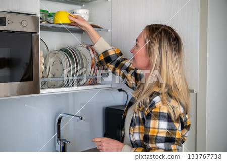 woman organizing clean dishes in kitchen cabinet woman organizing clean dishes in kitchen cabinet 133767738
