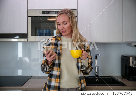 woman holding yellow cup and smartphone in modern kitchen 133767745
