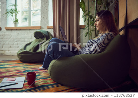 Woman working on laptop in cozy home interior with warm daylight 133768527